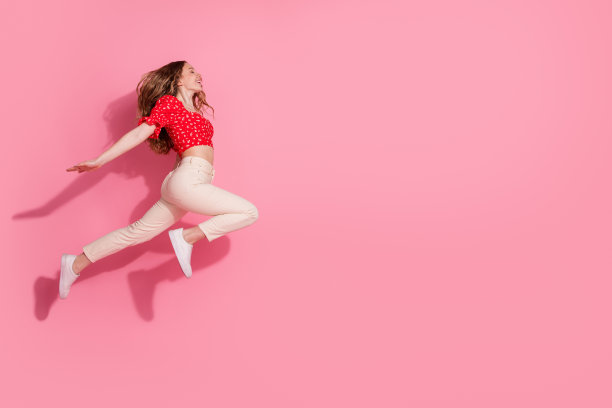 穿着时尚红色服装的漂亮少女在粉色背景上优雅地跳跃奔跑的全身照片图片下载