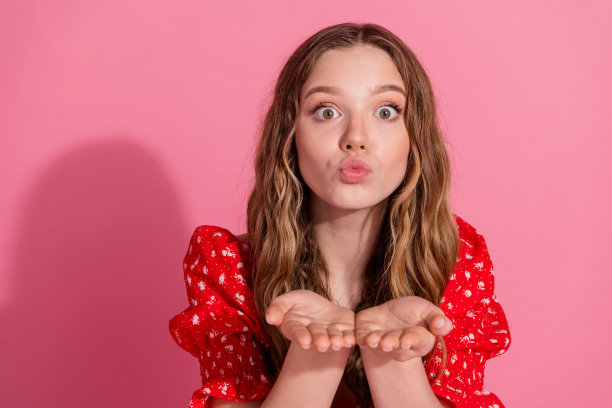 漂亮的少女在粉色背景下穿着时尚的红色服装，向你送出空气吻的照片肖像。图片下载