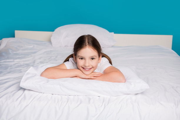 可爱的小女孩穿着睡衣，躺在枕头上，正在蓝色背景下的睡衣派对中入睡的全身照片图片下载