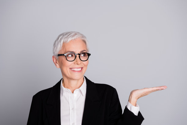 可爱的退休女性创业老板穿着正式服装，戴着眼镜，手持空白空间，独自站在灰色背景前的照片肖像图片下载