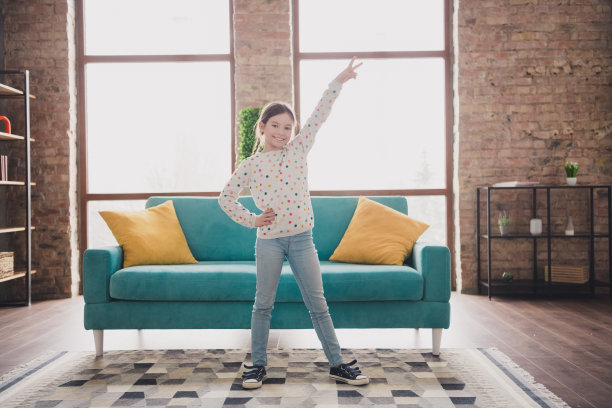 迷人的小女孩全身肖像，做出V字手势，穿着毛衣，现代室内公寓环境。图片下载