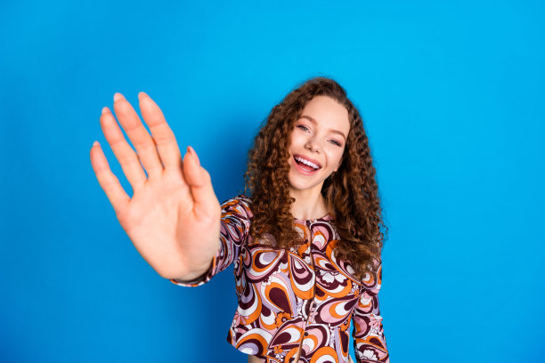 时尚多彩服装的迷人年轻女性在蓝色背景前挥手问好的人像照片图片下载