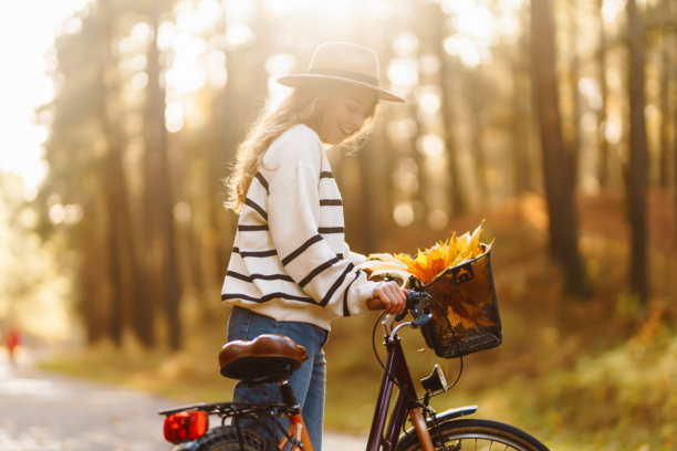 一位快乐的女性在阳光明媚的下午骑着自行车，沿着装饰着秋叶的如画森林小径。图片下载