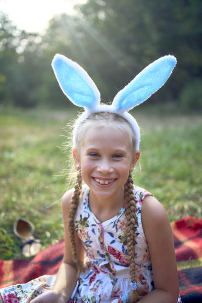 小金发女孩扎着辫子，戴着兔耳朵的复活节头饰，在公园里野餐。图片下载