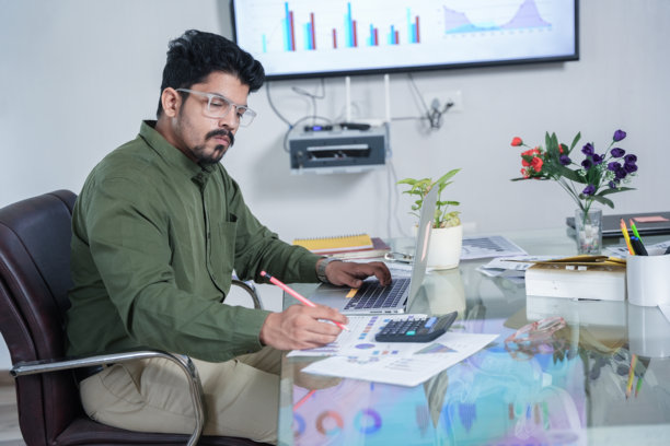 年轻的印度商人在办公室穿着正式服装，使用计算器处理公司报告。创业和财务规划概念。图片下载