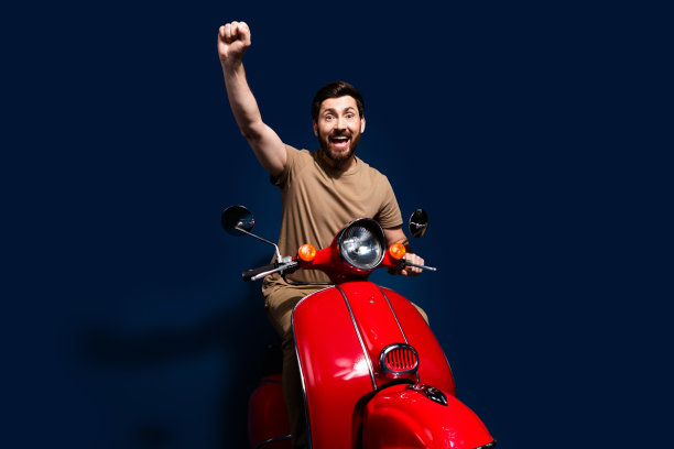 穿着米色T恤的快乐年轻男子在夏季骑摩托车，举起拳头，背景为深蓝色。图片下载