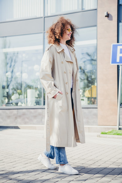 阳光明媚的春季户外，穿着时尚米色风衣的迷人快乐女孩的竖版照片图片下载