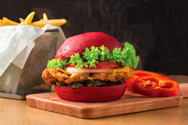 脆皮鸡肉汉堡配生菜、墨西哥辣椒、西红柿、奶酪，放在木板上，旁边有薯条篮，快餐的侧面视图图片下载