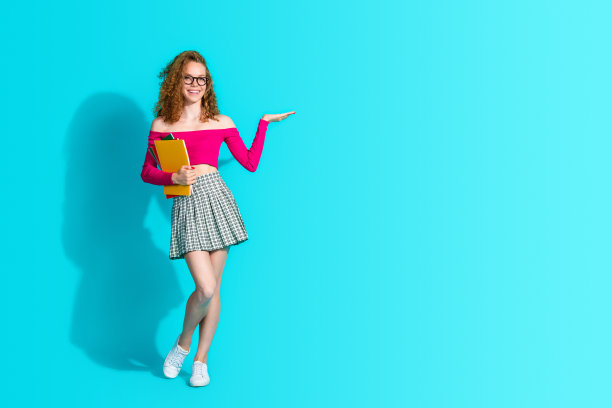 漂亮年轻女孩手持书本，穿着上衣，背景为青色，留有空白空间的全身照片图片下载
