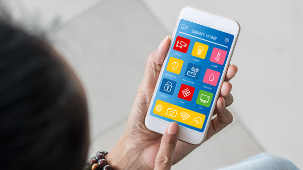 手持智能手机，运行智能家居应用，站立着。物联网（IoT）的概念。图片下载