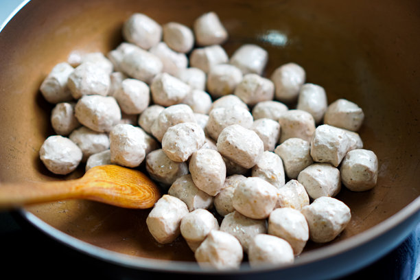 侧面照片显示厨师在家中用热电锅煎炸一组蘑菇素肉丸，家常素食。图片下载