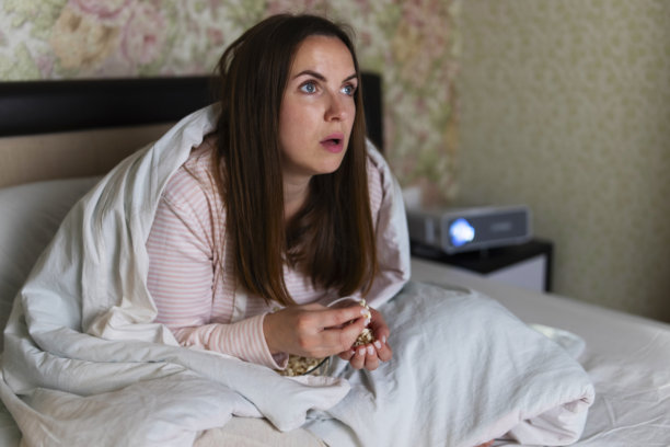 裹着毯子的女人在床上看电视图片下载