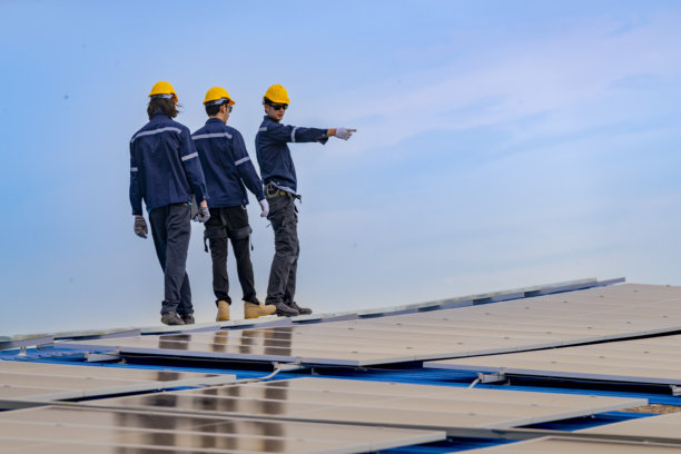 工人技术人员正在屋顶上安装太阳能电池板系统。男性技术人员在屋顶结构上行走，以检查光伏太阳能模块。图片下载