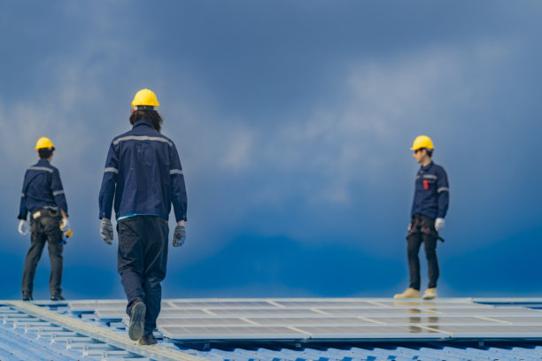 工人技术人员正在屋顶上安装太阳能电池板系统。男性技术人员在屋顶结构上行走，以检查光伏太阳能模块。图片下载