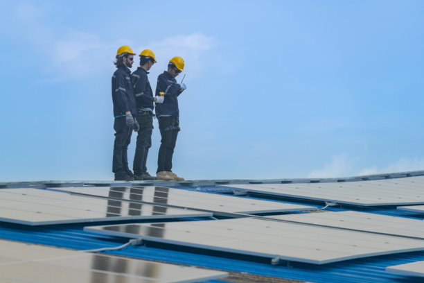 工人技术人员正在屋顶上安装太阳能光伏板系统。男性技术人员在屋顶结构上行走，以检查光伏太阳能模块。图片下载