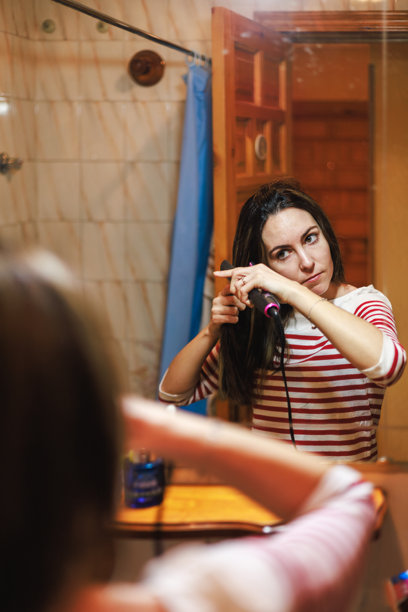 年轻的拉丁裔女性在乡村风格的浴室里使用卷发棒。图片下载