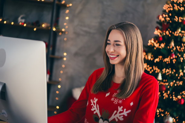 可爱的快乐女孩在室内房间里穿着圣诞服装，作为自由职业者在电脑上工作，营造出传统的节日氛围。图片下载