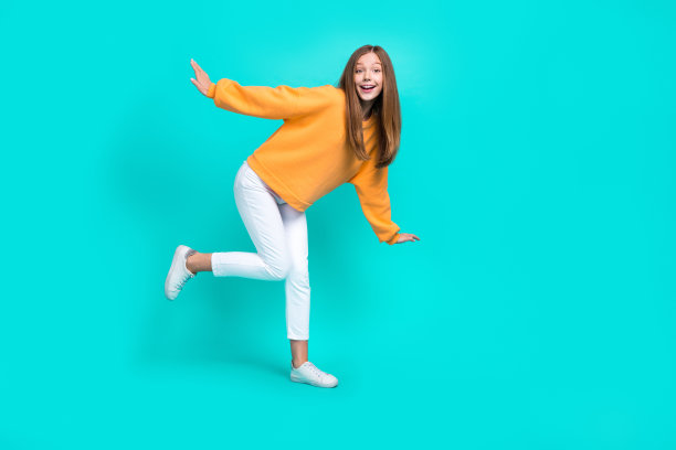 穿着橙色连帽衫的可爱小女孩在空旷的空间中玩耍，背景为青色。图片下载