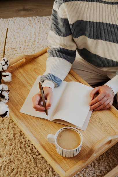 舒适的写作环境，木托盘上放着咖啡。一位女性在笔记本上写字。非常适合舒适、生产力和灵感的主题。图片下载