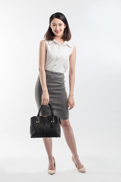 一位身着商务装的亚洲年轻女性拿着黑色手提包，对着镜头微笑图片下载