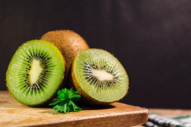 深色背景下的木桌上放着绿色猕猴桃和切片猕猴桃图片下载