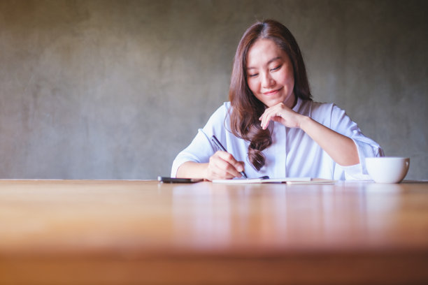 一位女性在木桌上写笔记，旁边有手机和咖啡杯的肖像照片图片下载