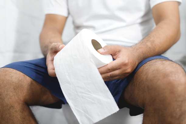 男子因腹泻而痛苦，手中握着卫生纸卷，坐在马桶前。卫生间里的便秘。治疗腹痛和卫生保健。图片下载