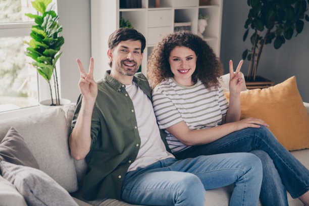 两个年轻人在现代公寓内沙发上展示V手势的照片图片下载