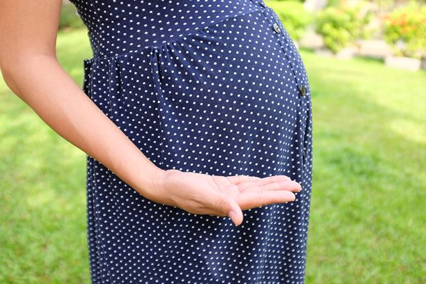 特写孕妇在花园中用手托着肚子，手中拿着广告概念的物品。图片下载