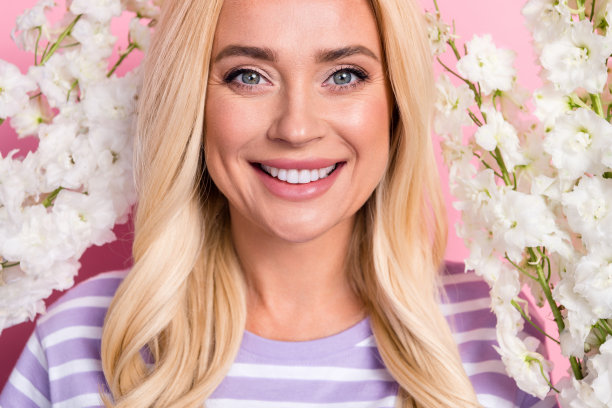 特写照片，迷人的可爱女士在春季公园的白色花朵中微笑着走，背景为粉色。图片下载