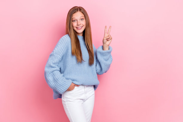 穿着时尚服装的女士举起手臂，做出V字手势，粉红色背景图片下载