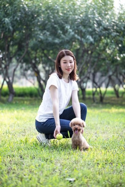 一位年轻女性正在公园里和一只贵宾犬玩耍图片下载