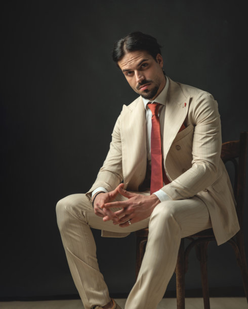 沉思的时尚男士穿着米色西装坐在木椅上图片下载