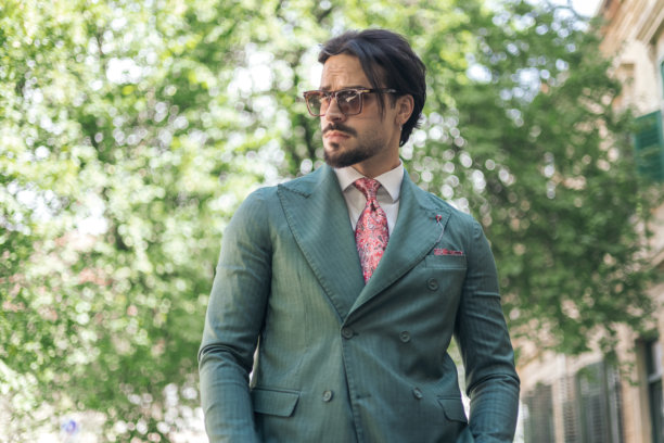 自信的时尚男士穿着绿色西装，戴着太阳镜，侧目而视。图片下载