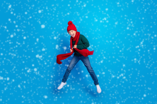 穿着冬季衣物的男孩在明亮的蓝色背景上跳跃的全身照片图片下载