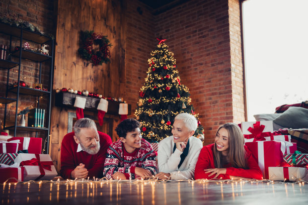 可爱的家庭照片，祖父、祖母、孙子和孙女躺在圣诞树旁的地板上，欣赏家中的装饰。图片下载