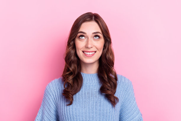 特写照片：年轻、积极、微笑的可爱卷发女孩穿着蓝色针织毛衣，仰望着梦想中的黑色星期五，背景为粉色。图片下载