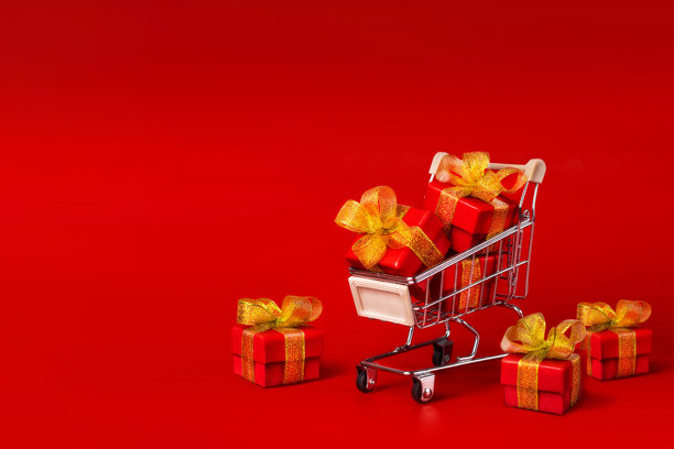 一个装满红色礼物和金色蝴蝶结的购物车，背景为红色。节日，礼物，购物，留白。图片下载