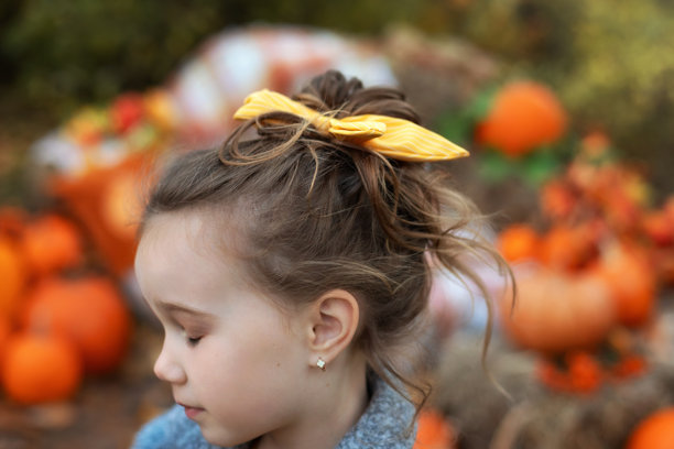 金发小女孩将她的波浪卷发扎成低马尾，配上时尚的发饰。背面和侧面特写。马尾与发饰。小女孩的肖像，头上戴着黄色雪纺发饰。图片下载
