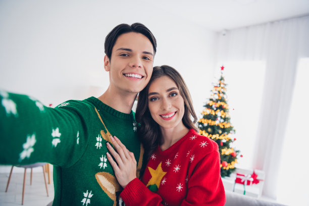 年轻情侣在圣诞树灯光装饰下的室内浴室拍摄的自拍特写照片，享受冬季假期的温馨时光。图片下载