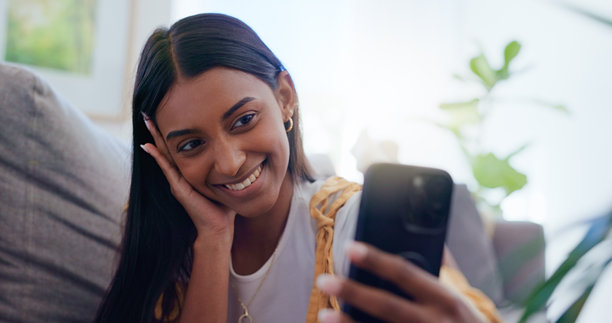 自拍，家中女子坐在沙发上，放松愉快，享受社交媒体，幸福感满满，互联网在客厅中。这个人，公寓里的女孩手持手机，面带微笑，开心地更新个人资料照片。图片下载