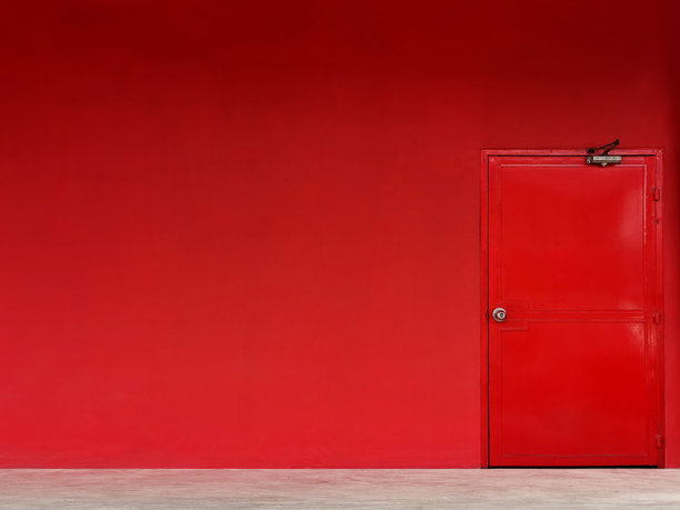 红色墙壁上的红色入口门。房间里的彩色门。图片下载