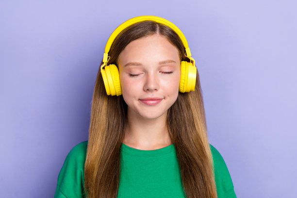 特写照片，漂亮可爱的女士穿着绿色时尚服装，闭着眼睛，佩戴高品质耳机，背景为紫色。图片下载