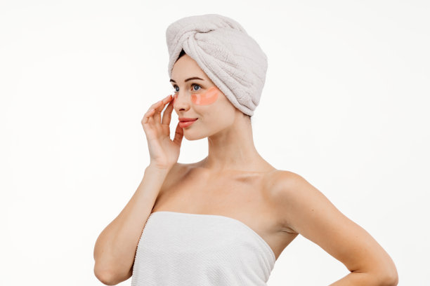 年轻女性的特写，使用眼部贴片针对皱纹和黑眼圈。背景为白色，这张图片强调护肤和对抗疲劳迹象。图片下载