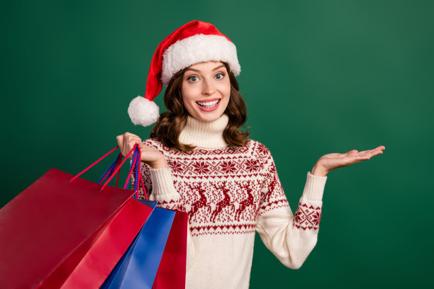 拿着包裹，手臂指向空白区域，展示新年优惠的漂亮女士照片，绿色背景图片下载