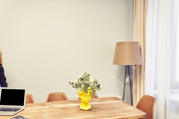明亮的办公室内部，摆放着干花和一台笔记本电脑。木质办公桌上的黑色笔记本电脑屏幕，位于一个时尚的房间内，白色墙壁和留白空间。图片下载
