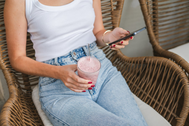 女人在阳台上使用智能手机并喝草莓冰沙图片下载