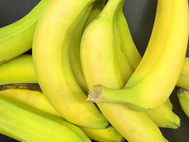 超大画幅的超市展示架，黑色货架上摆放着一堆成熟的黄色香蕉（芭蕉），水果堆的手，黑色背景，前景聚焦。图片下载