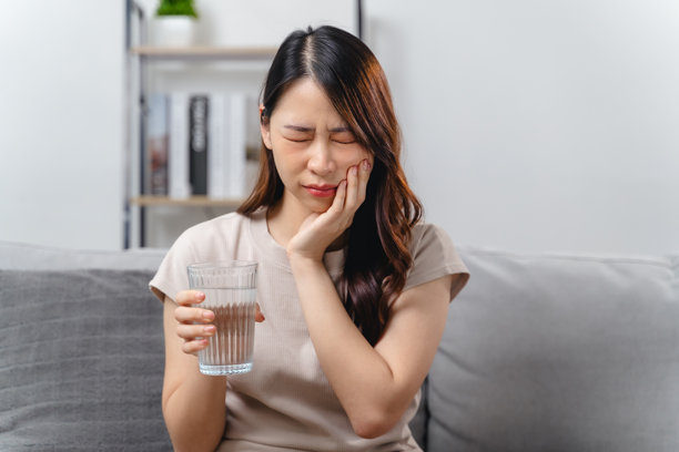 女人坐在沙发上，拿着一杯水，牙疼图片下载