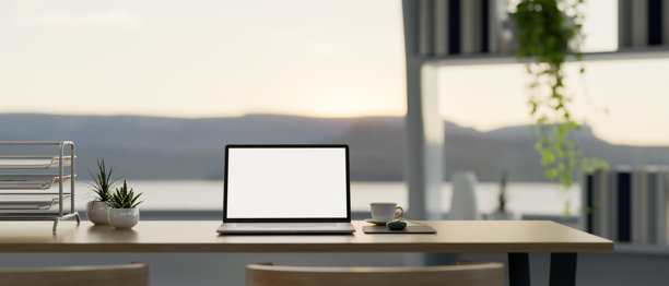 现代办公室的木质桌子上放着一台笔记本电脑，窗外有自然风景的大窗户。图片下载